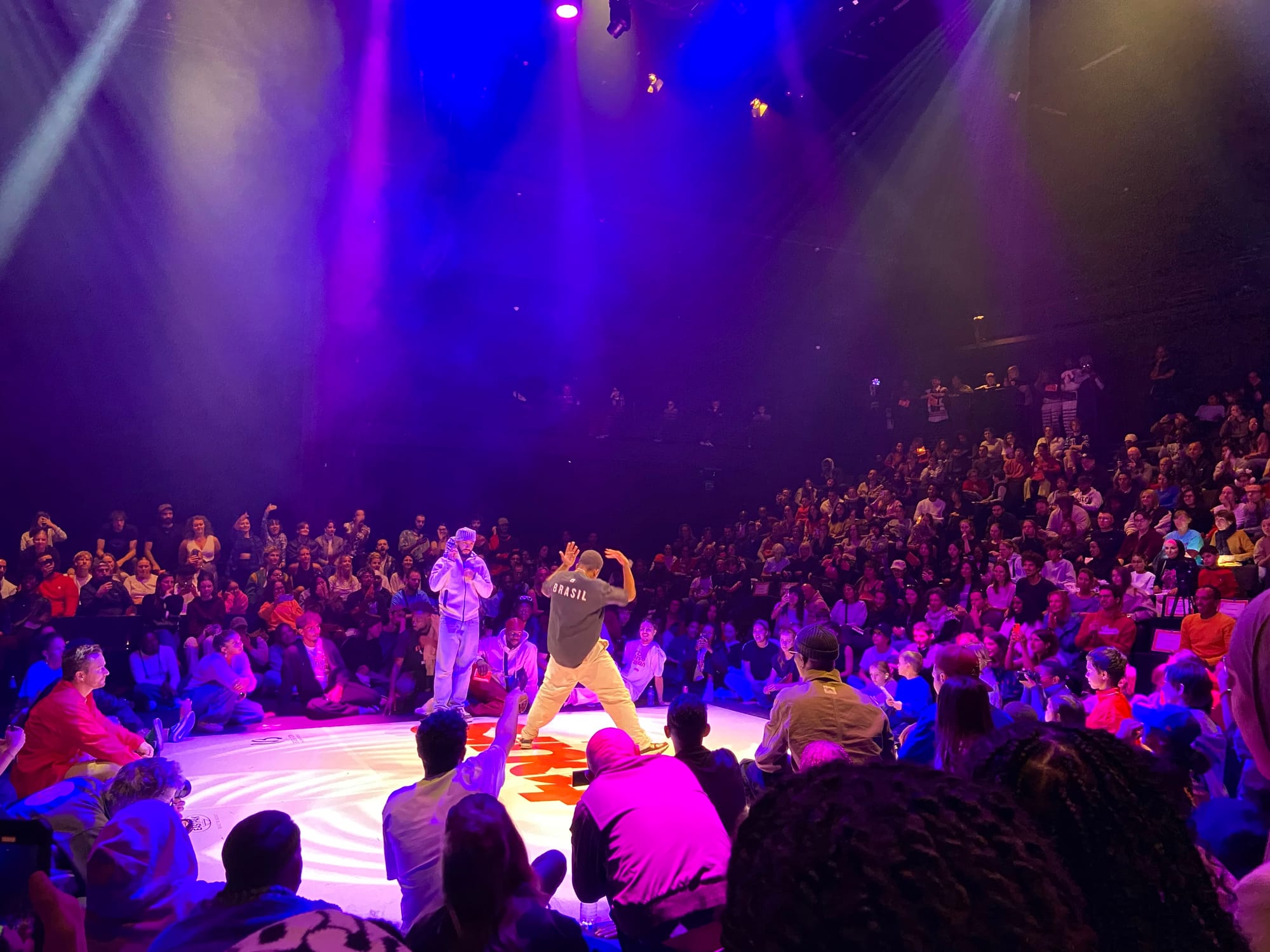 There are two dancers in the middle of the dance floor surrounded by people sitting. There are also people in the bleachers.