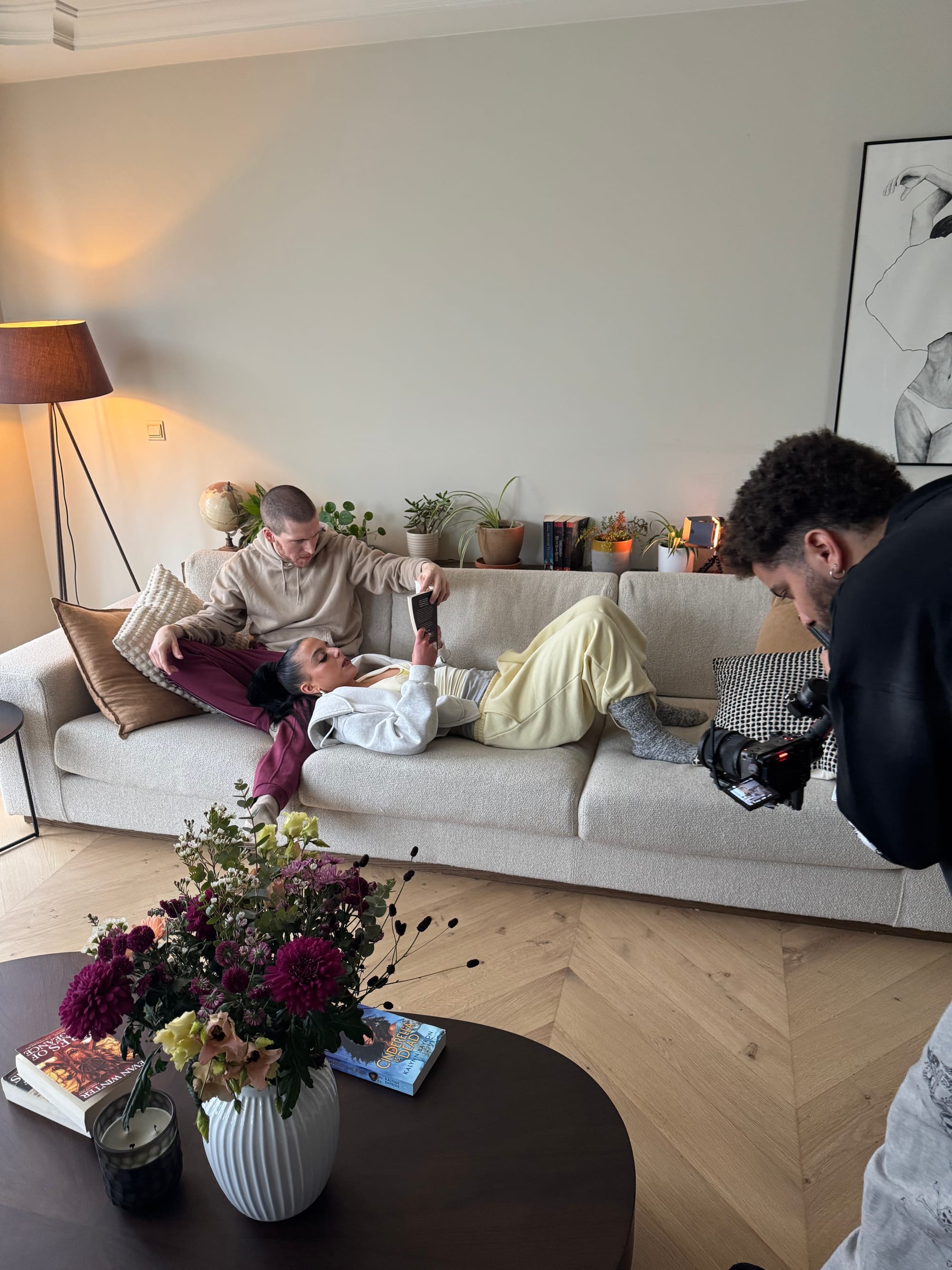 Slim B and Pippa are sitting on the couch and reading a book while Adam is filming them.