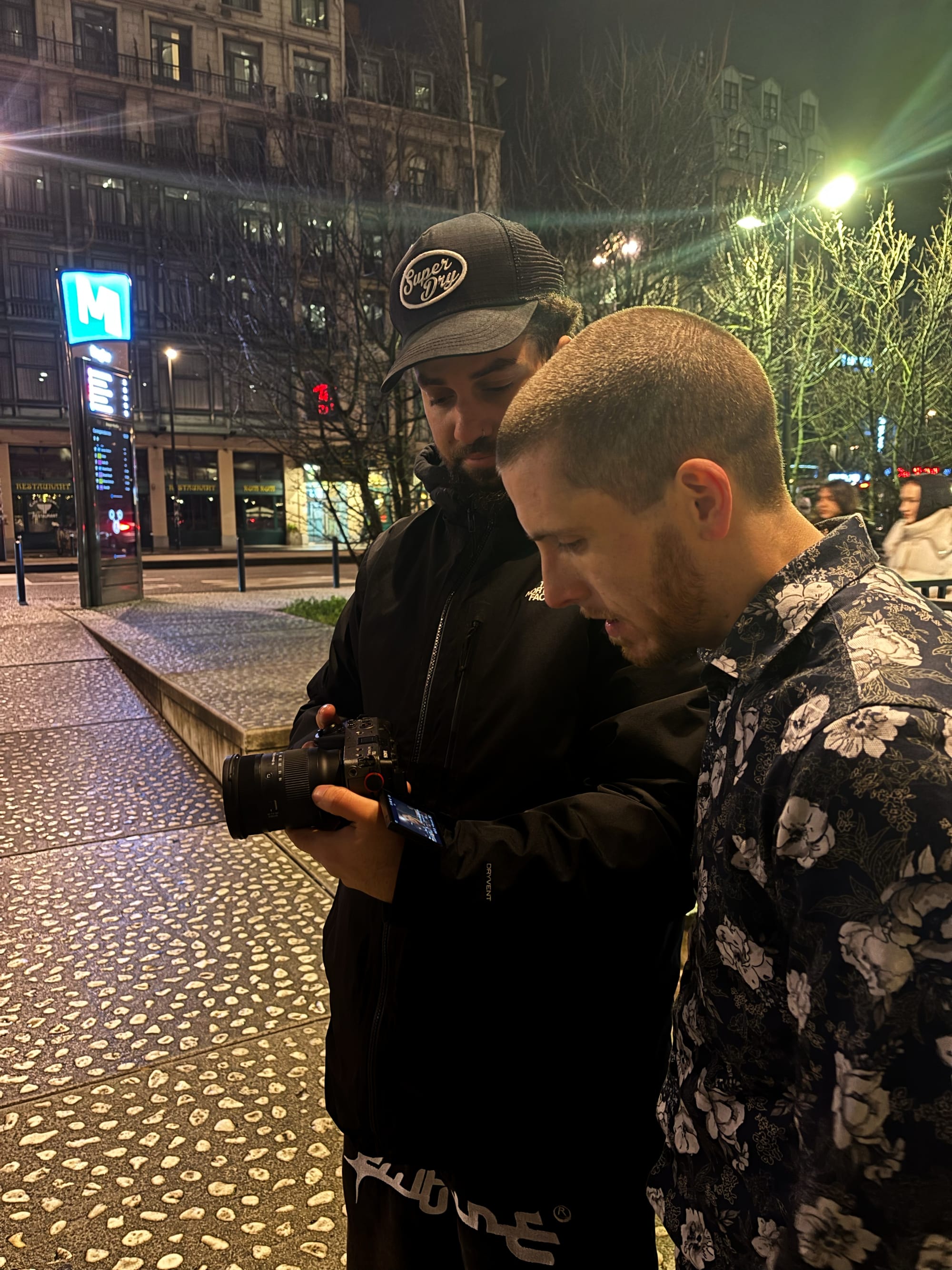 Adam and Slim B are watching a take on the camera. They are outside in Brussels at night.