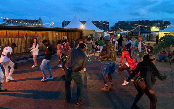 People dancing outside on a wooden floor at a festival on a beach in the evening