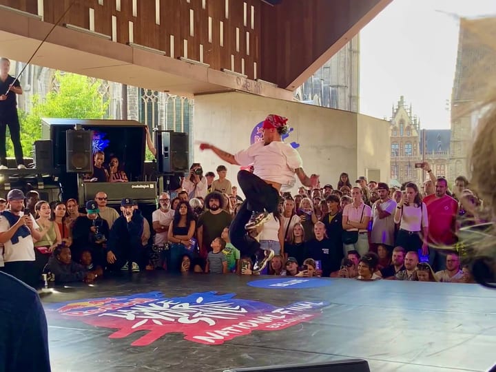 A dancer is on a stage surrounded by people, under a covered area. The DJ booth is the on the left side.