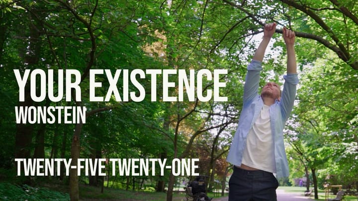 Slim B is on a road between trees in a park. He is reach to the sky with both arms, while wearing a white t-shirt, a light blue button-up shirt, and dark blue pants.
