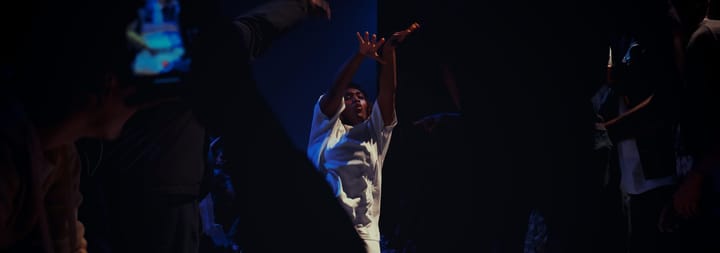 Kassy is dancing during the exhibition 5 vs 5 battle. She is surrounded by the other dancers and the audience.